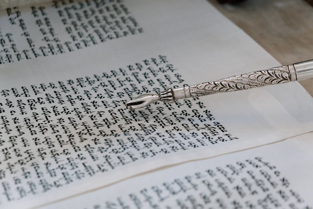 A detailed view of a silver yad pointing to Hebrew text in a Torah scroll.